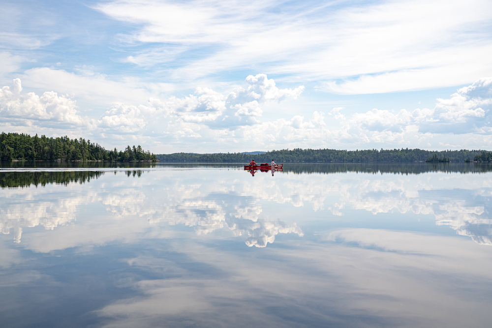 Red canoe being paddled on mirror-like lake