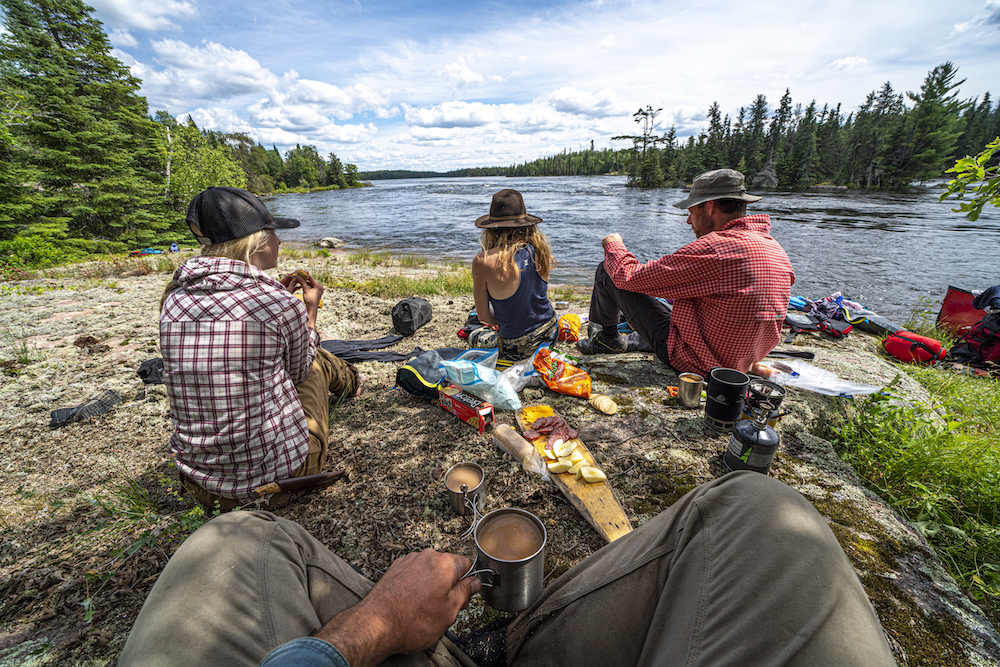 Four people sitting with a spread of food on shore 