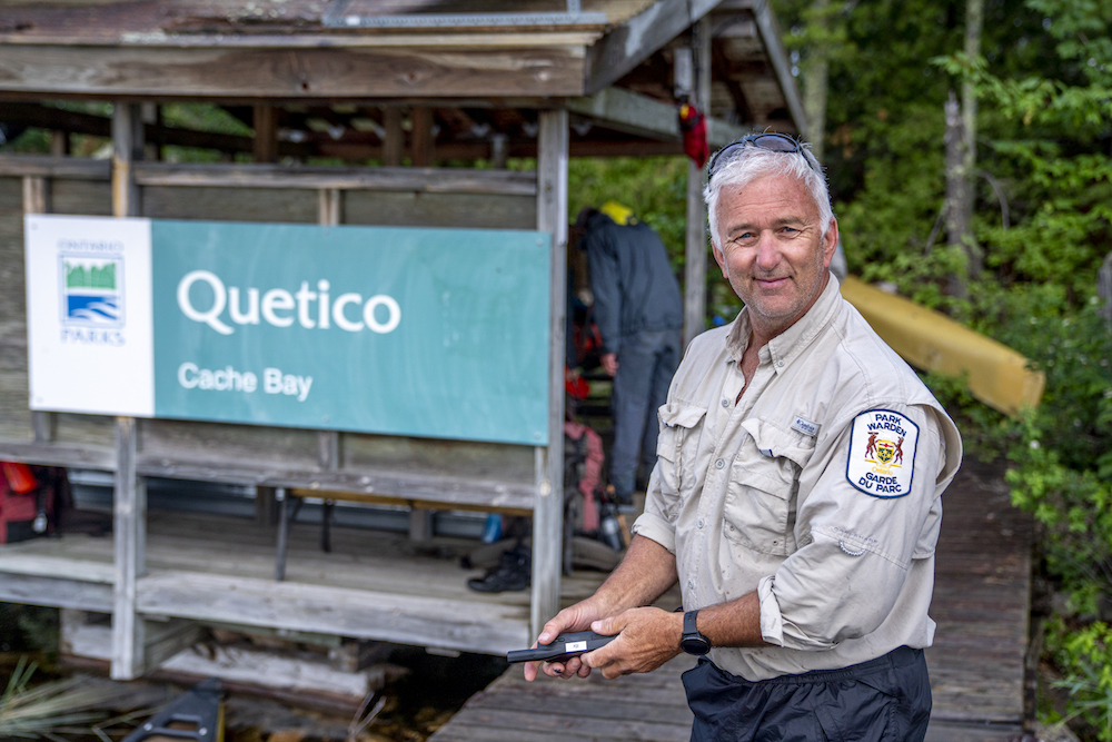 Quetico Park staff stands on dock in front of Quetico sign.