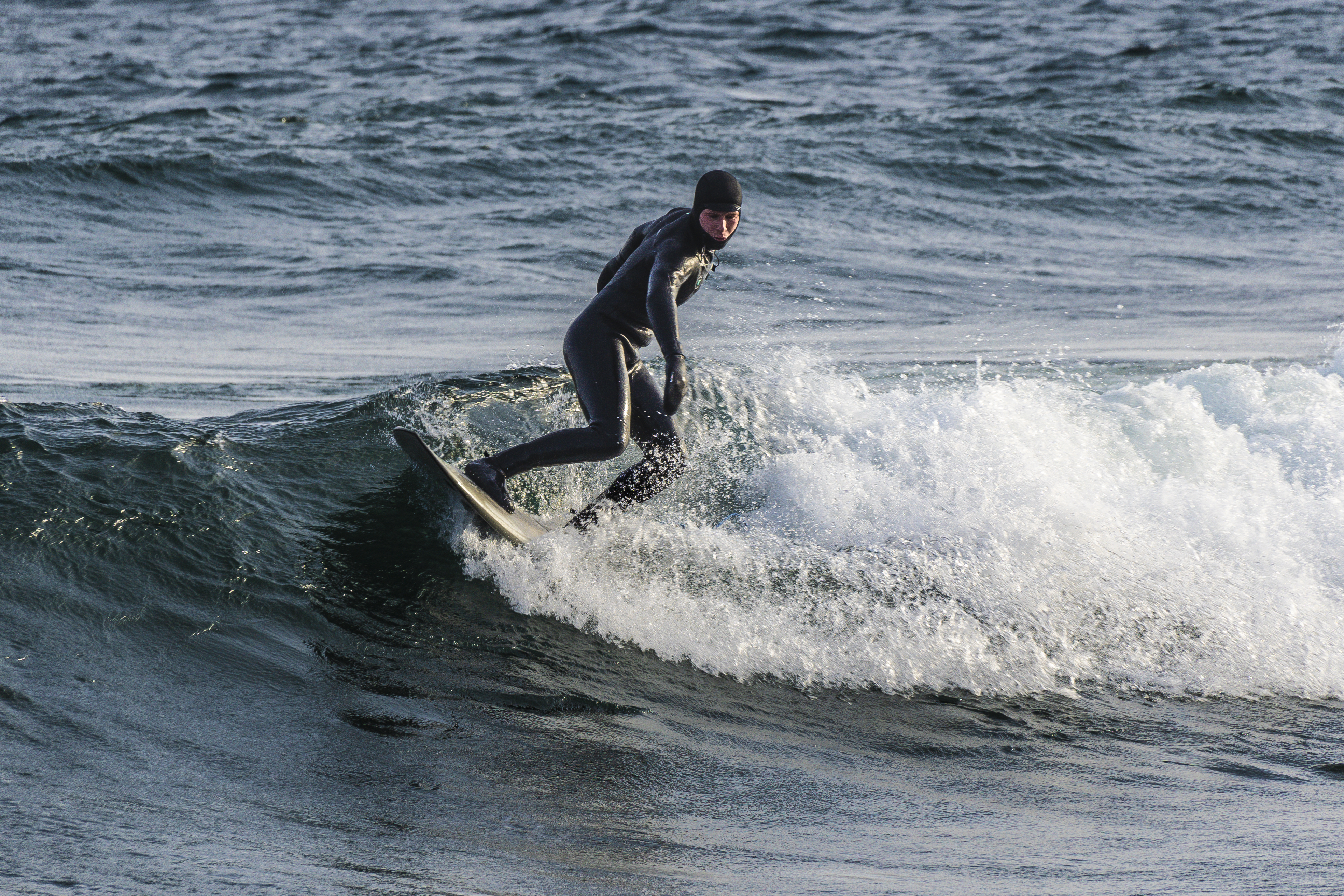 a person in a black wetsuit surfs on white-capped lake waves under a blue sky