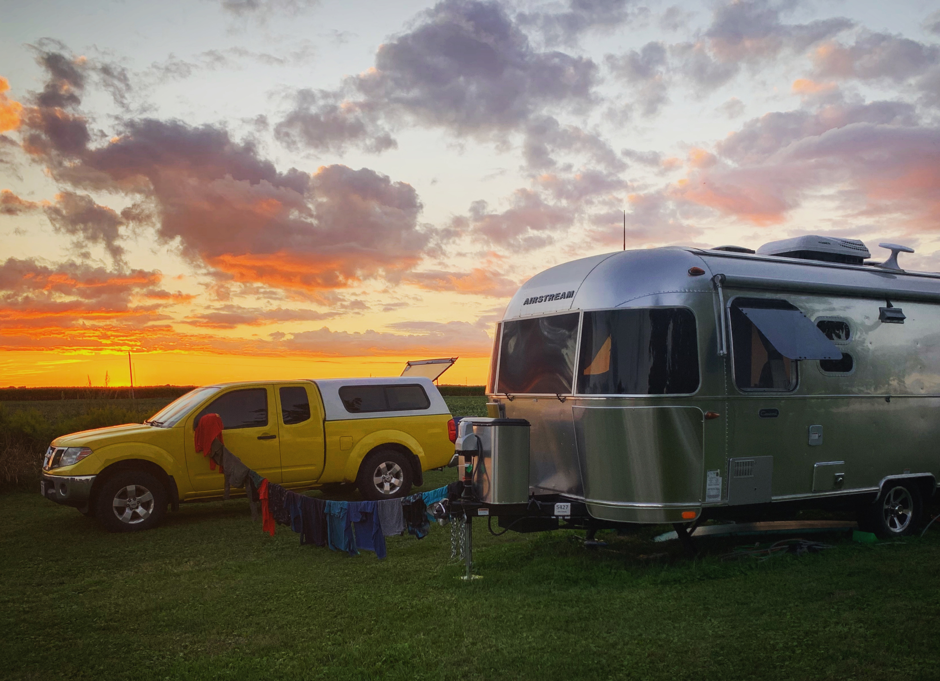 An RV with a sunset in the background and a clothesline with clothing. 