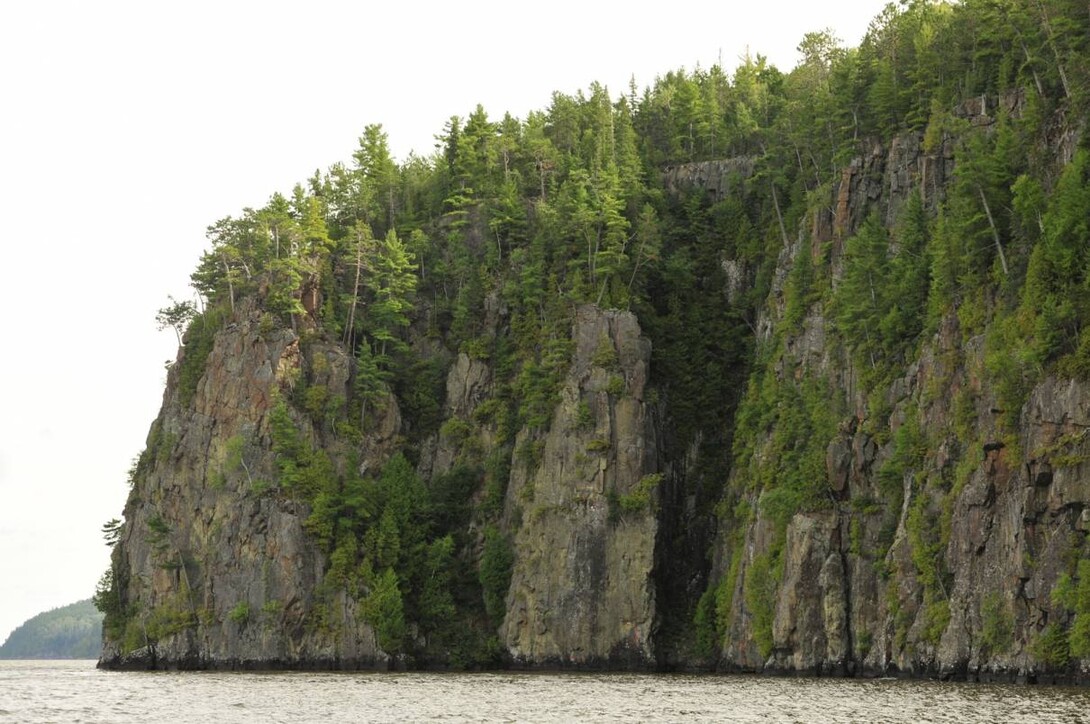 A tall sheer cliff rising out of a lake.