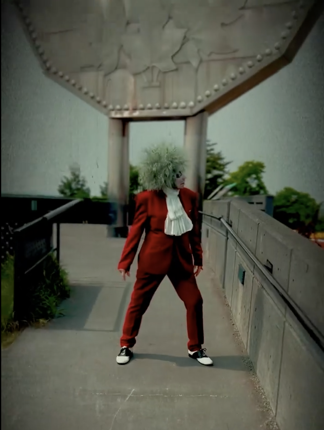 An actor in a red suit, dressed up like the character Beetlejuice, dancing in front of the Sudbury Big Nickel statue