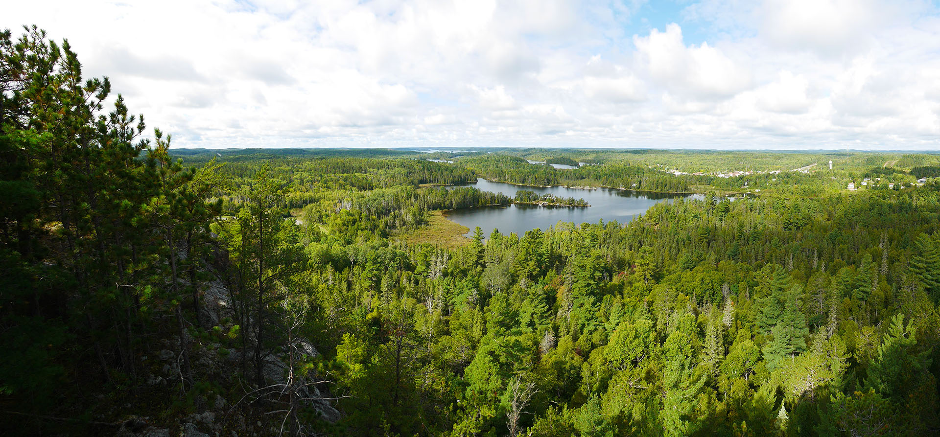 a view of a green forested valley with a blue lake in the far distance