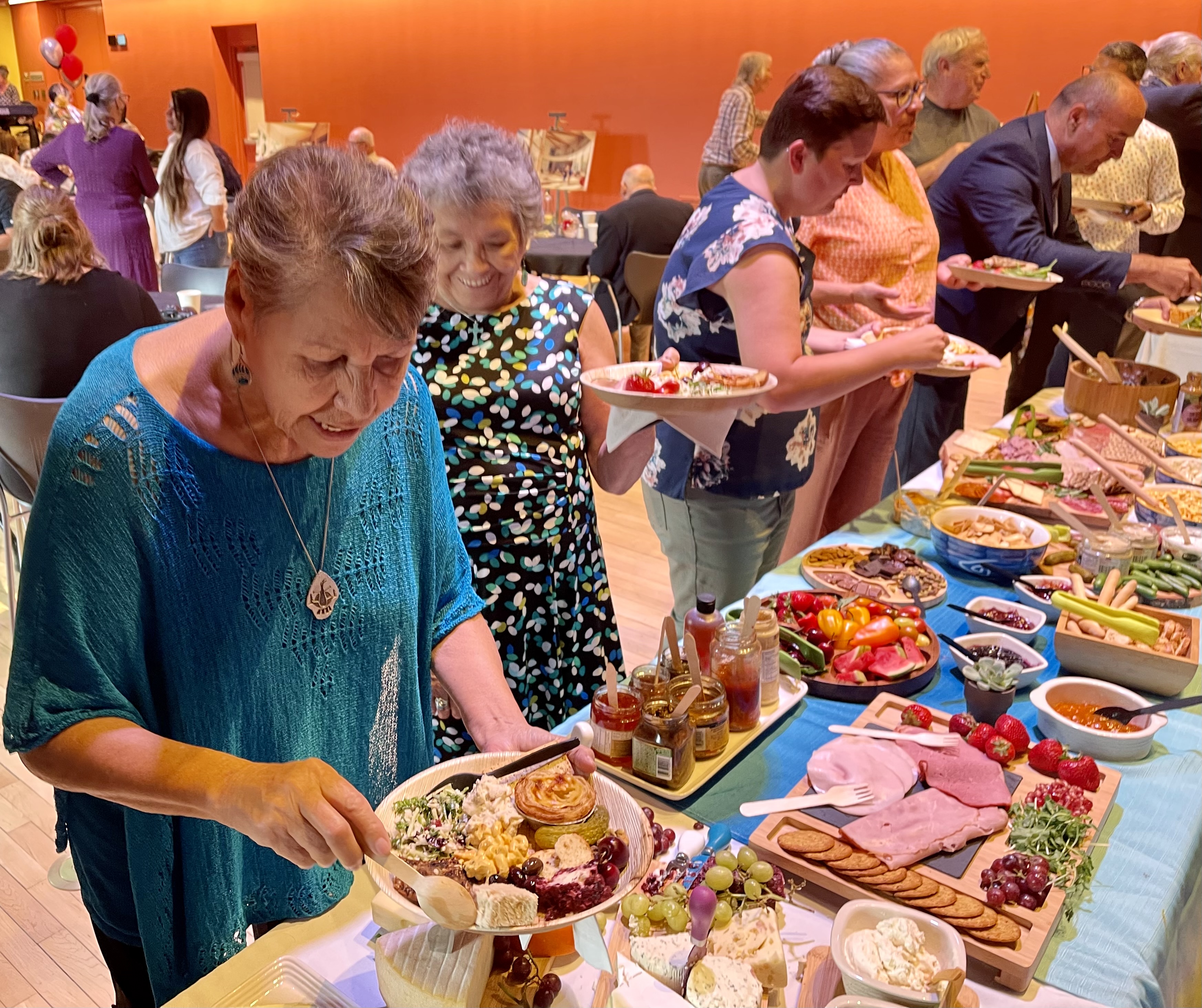 many smiling people filling their plates at a delicious-looking buffet