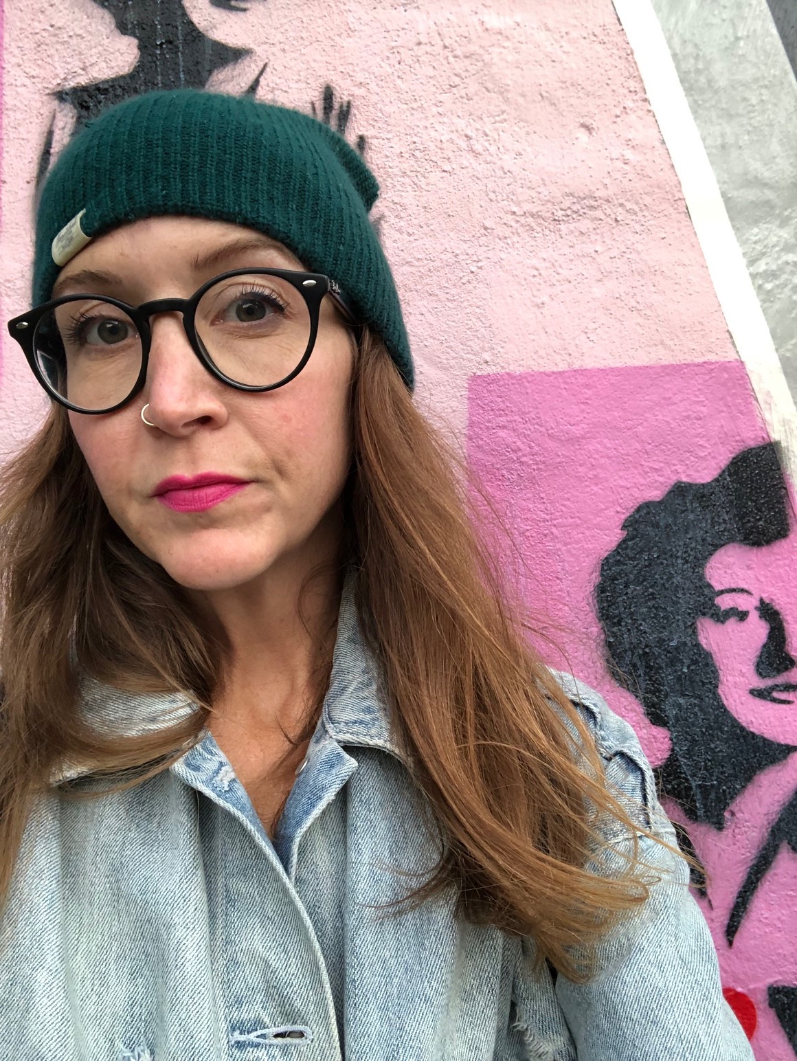 Jaymie Lathem wearing a black toque and glasses in front of a pink painted wall