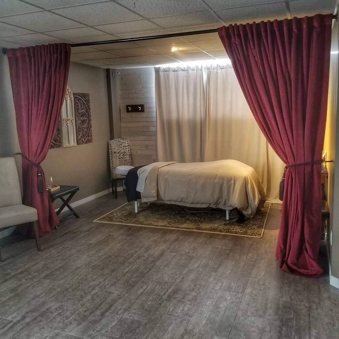 A white spa bed in a clean room with a wooden floor, decorated with red and cream curtains and white chairs