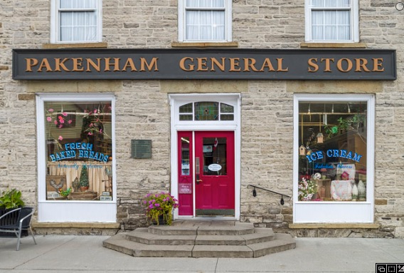 a pretty antique stone building with a red door and white-trimmed windows, with a sign that says "Pakenham General Store"