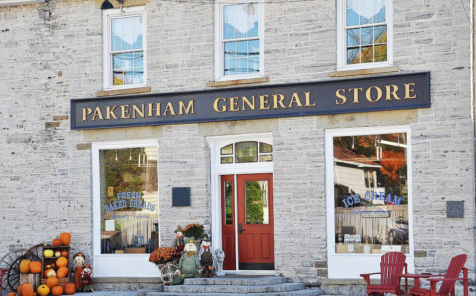 the exterior of the Pakenham General Store, an old white stone building with a red door, and a sign for fresh baked bread in the window