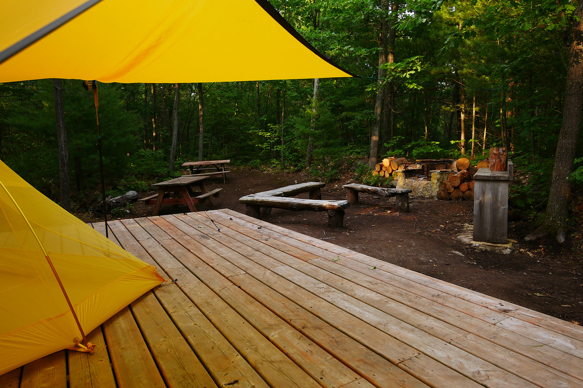 A wooden deck and yellow tent set among a clearing of trees in Point Grondine Park.