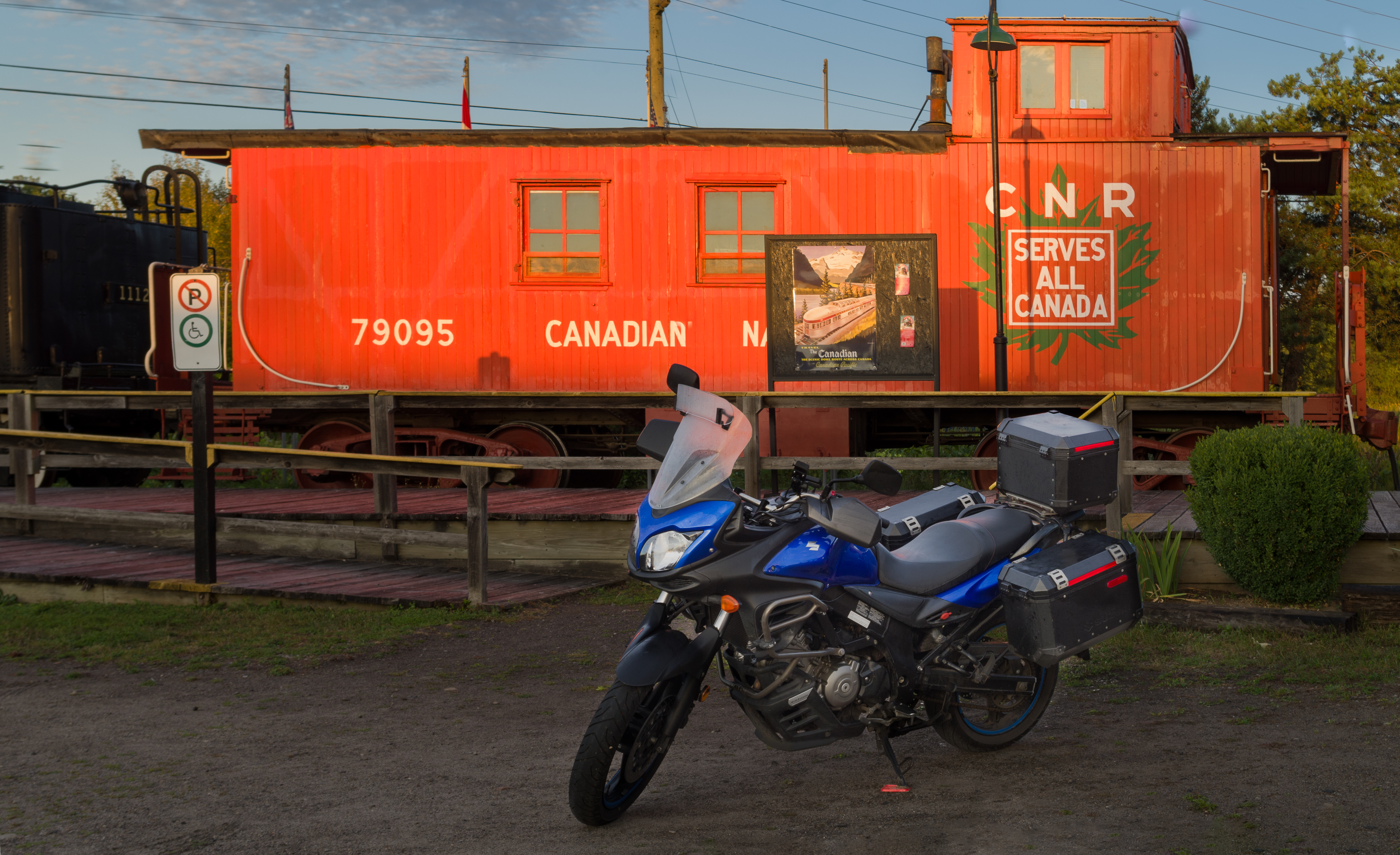 A blue motorcycle parked next to a bright red train caboose car at dusk
