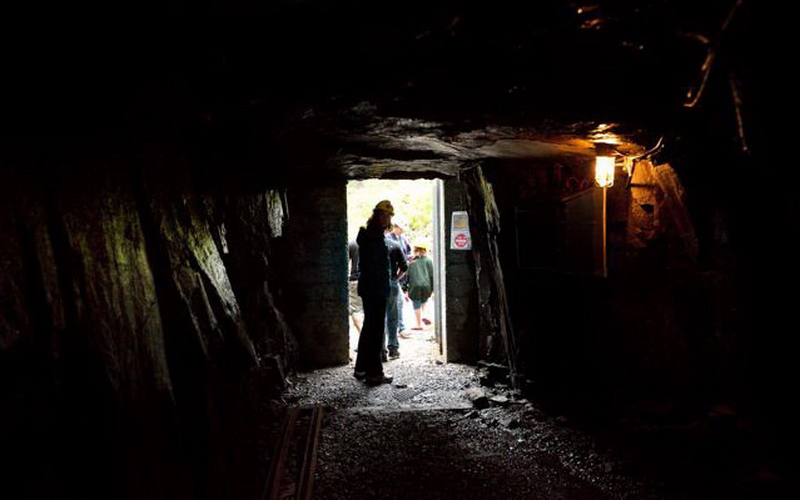 A visitor wearing a mining helmet in a dark mineshaft on a guided tour of Colonial adit