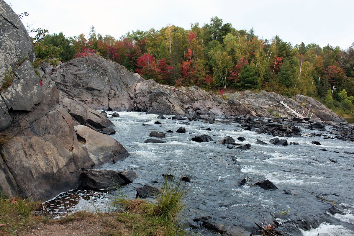 A view of the river at Chutes Provincial Park; a rocky river with steep stone banks and red and green autumn trees in the background.