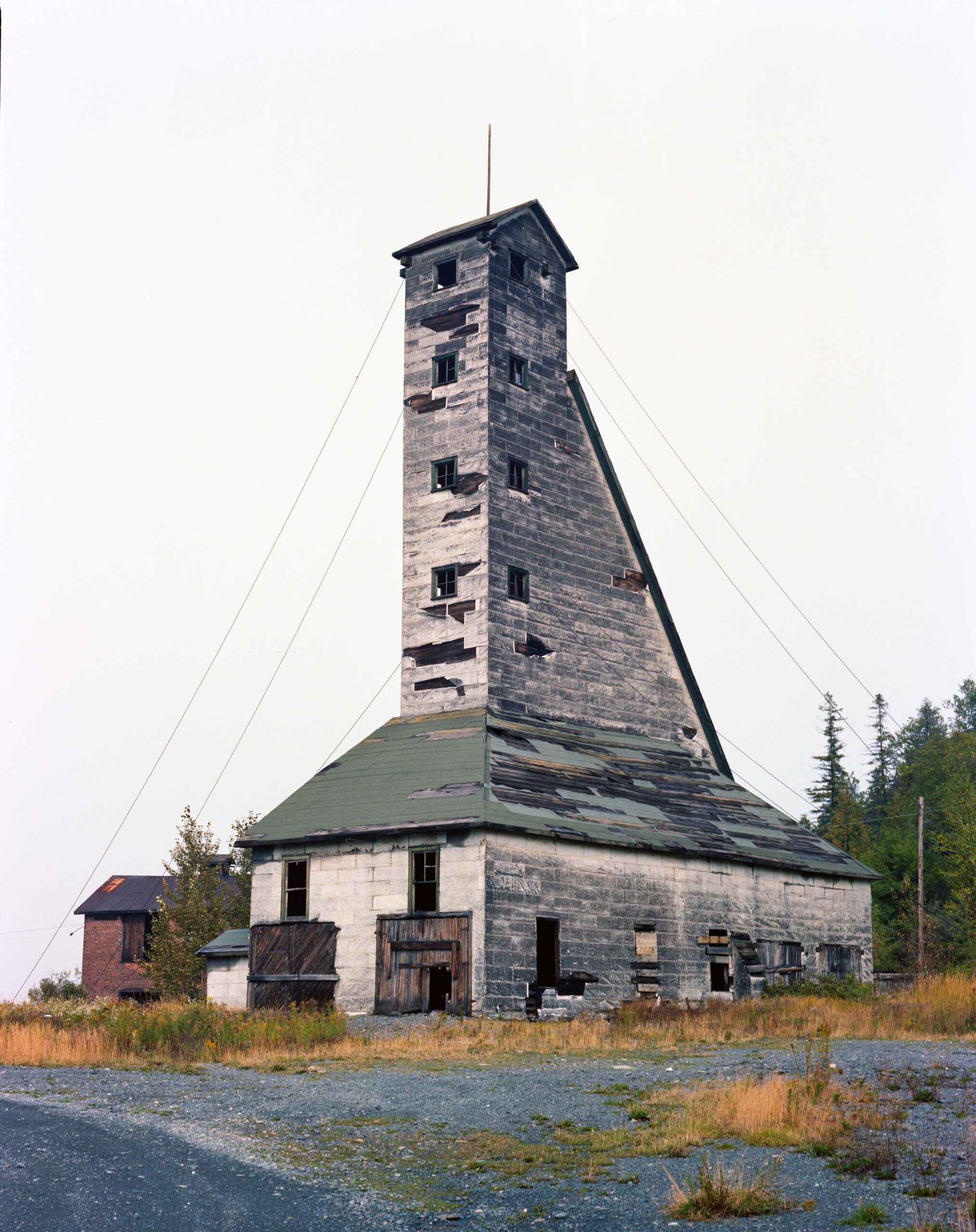 the Colonial Mine headframe; a tall white and green headframe building, severely weathered and with boarded windows, surrounded in dry autumn grass and brush.