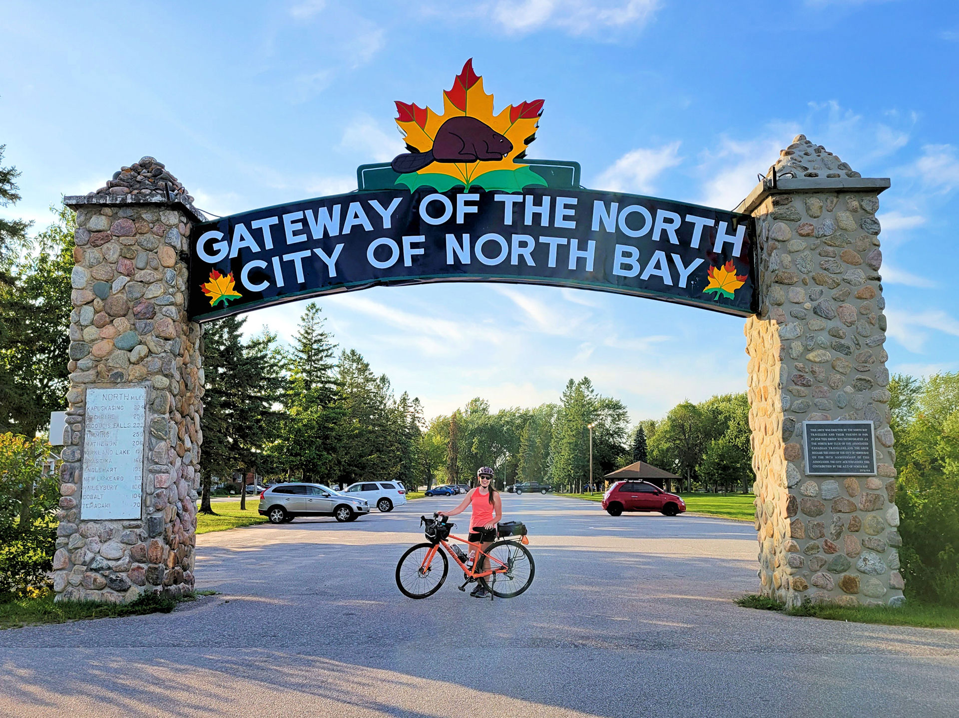 woman poses with bicycle in front of the Welcome to North Bay sign