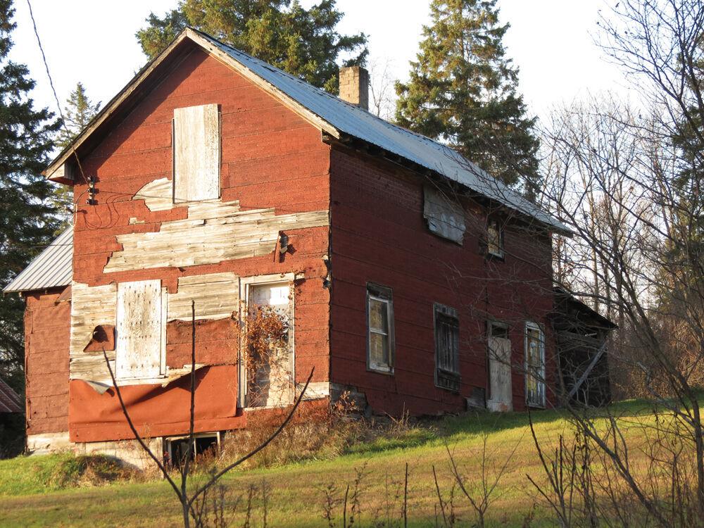 a weathered and abandoned red wooden building, surrounded in trees