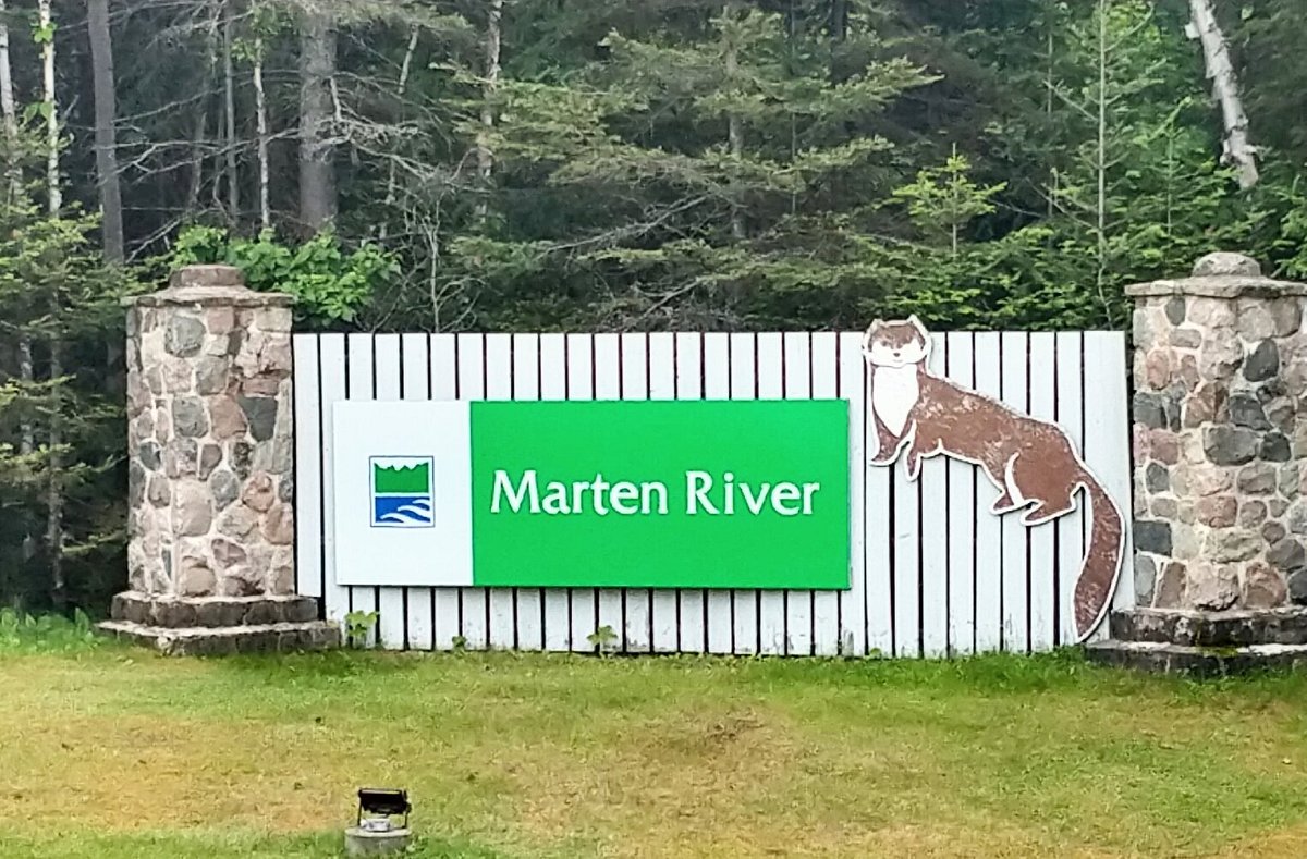 a large white and green sign with stone end-pillars, a large painted marten and Ontario Parks logo on it, that reads "Marten River". There is green forest in the background.