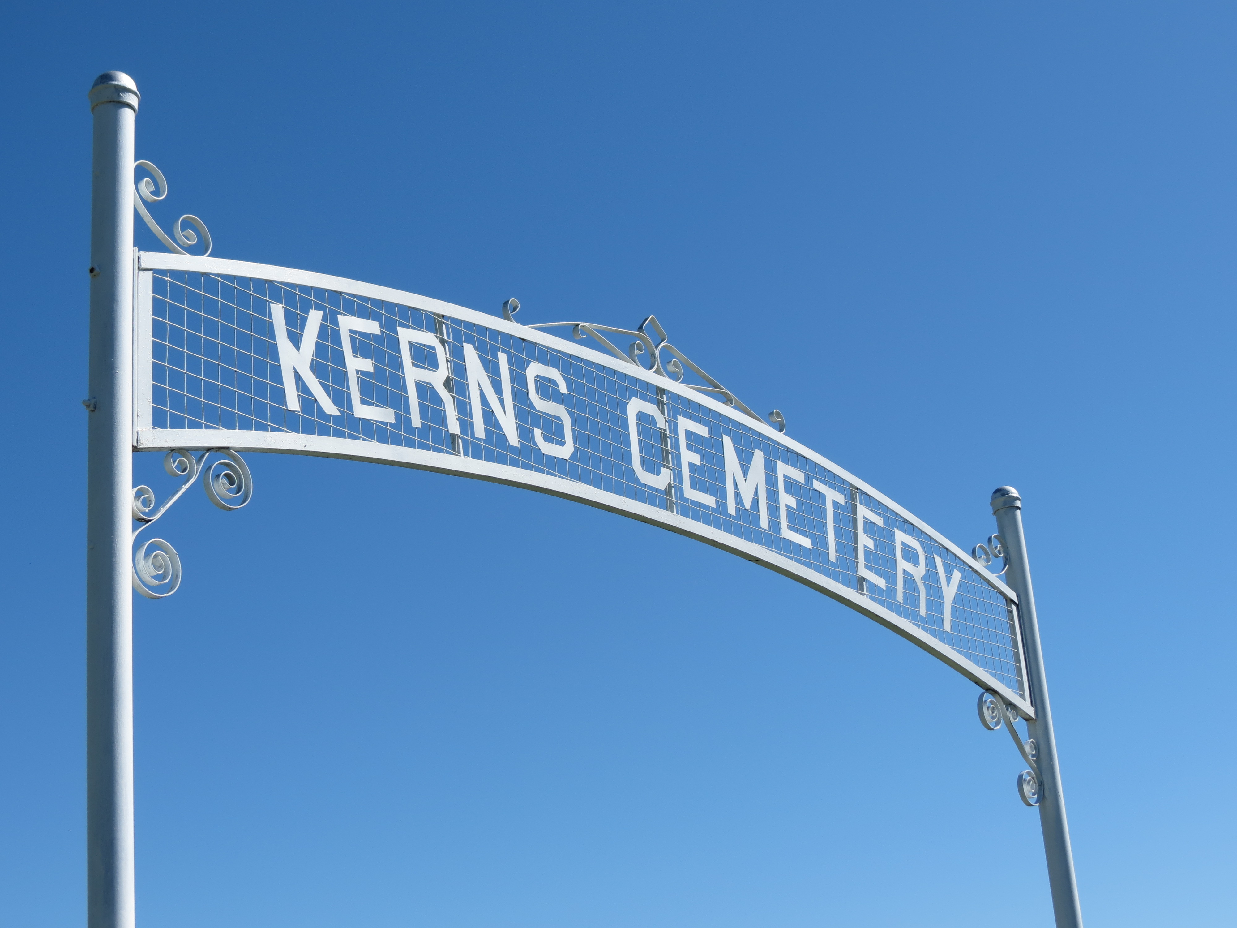  A tall white metal gateway that says "Kerns Cemetery", in front of a dusky blue sky.