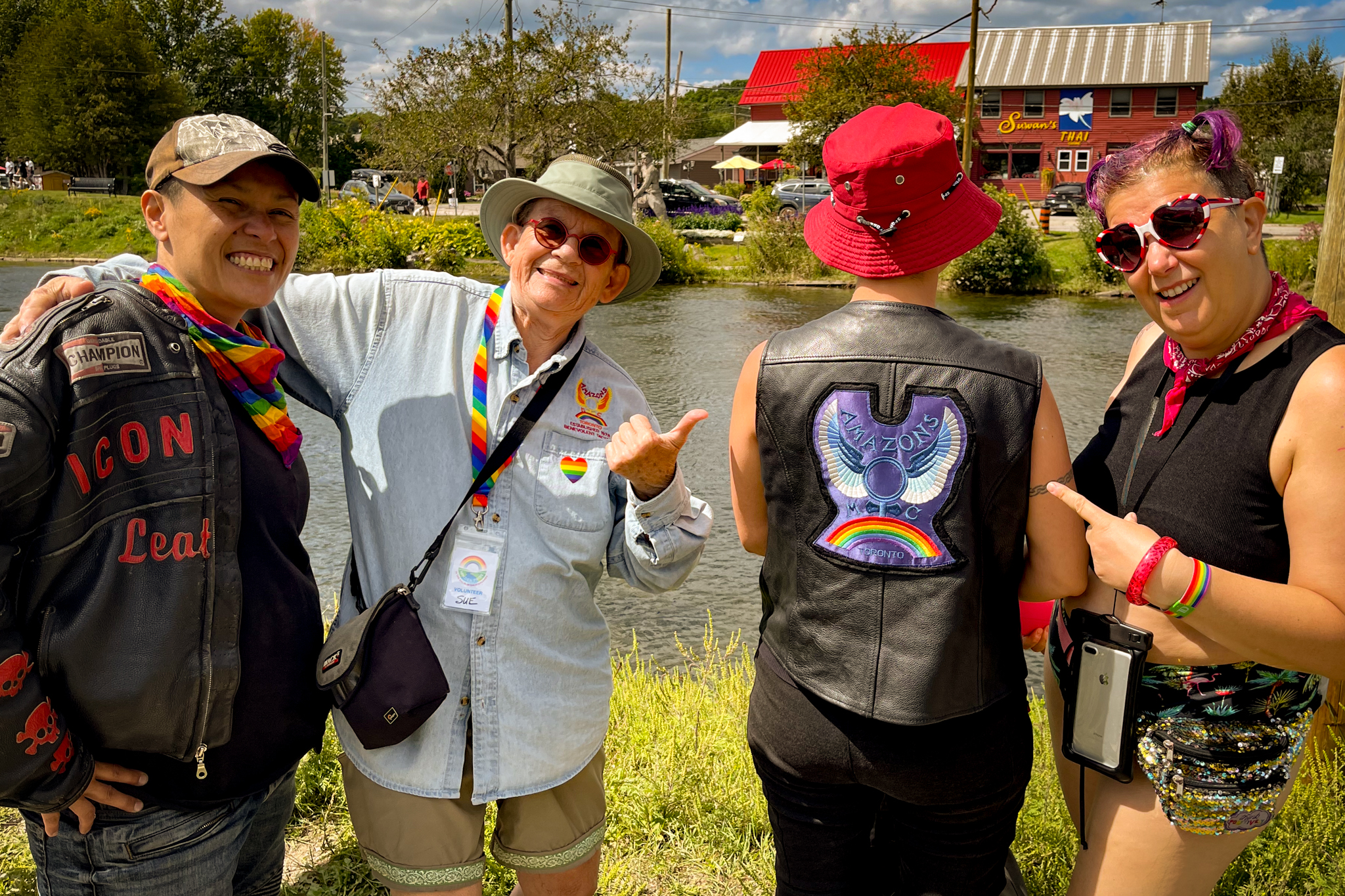 3 smiling people pointing at the large rainbow and purple "Amazons" patch on the back of a forth person's vest.