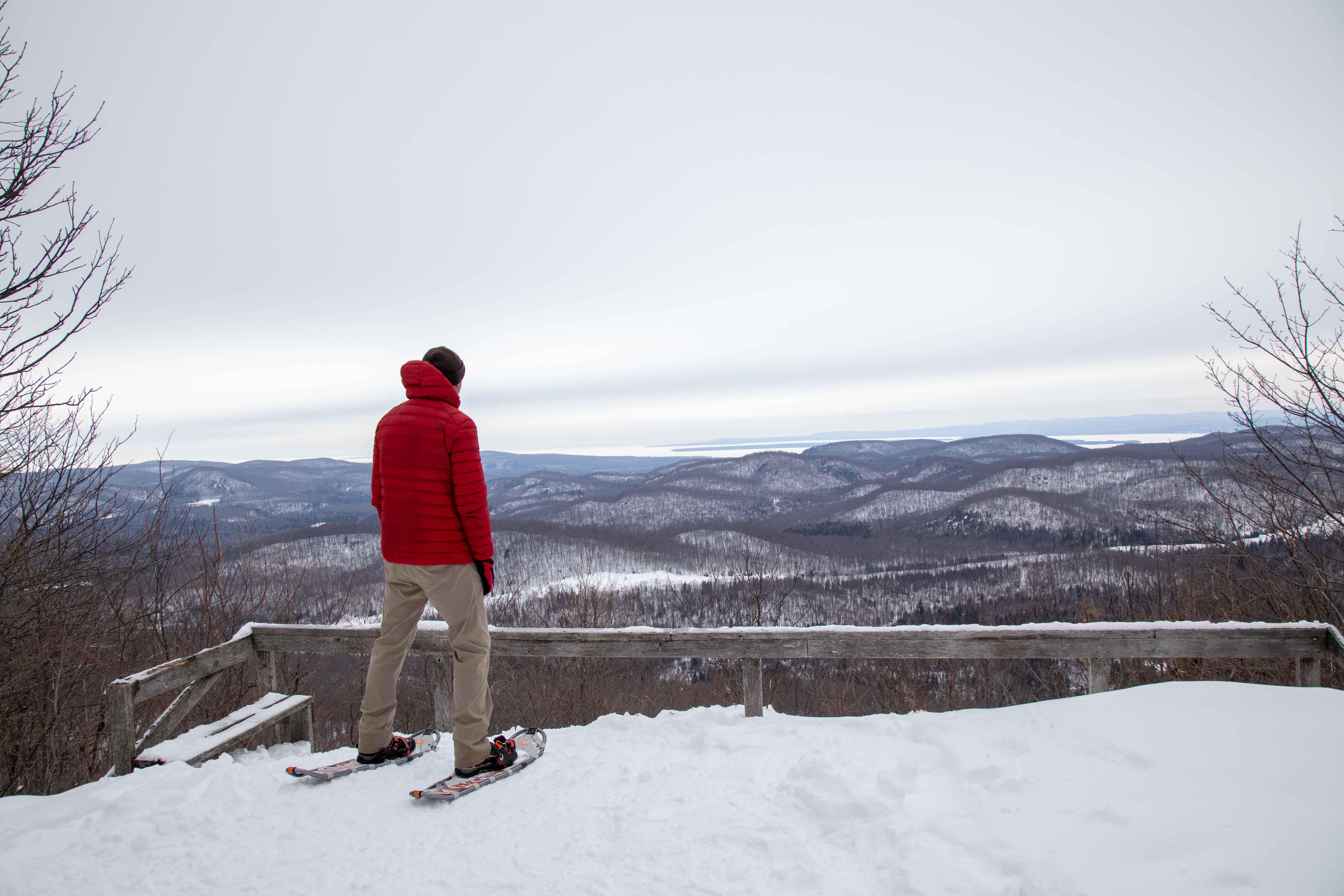a person wearing snowshoes looks out at a hilly winter view