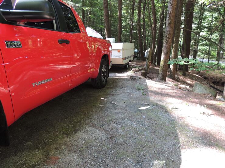 a red pickup pulling a camper parked in a heavily treed campsite
