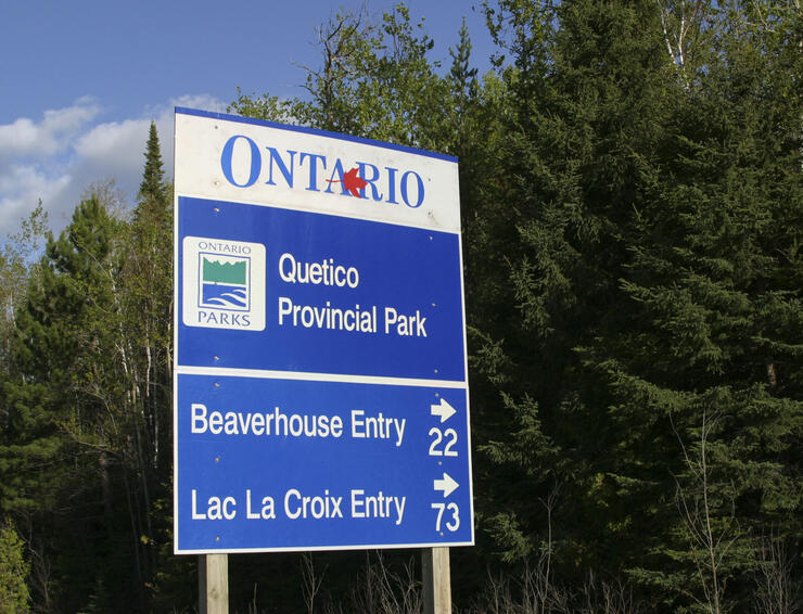 a blue road sign that says "Quetico Provincial Park", with green spruce trees in the background