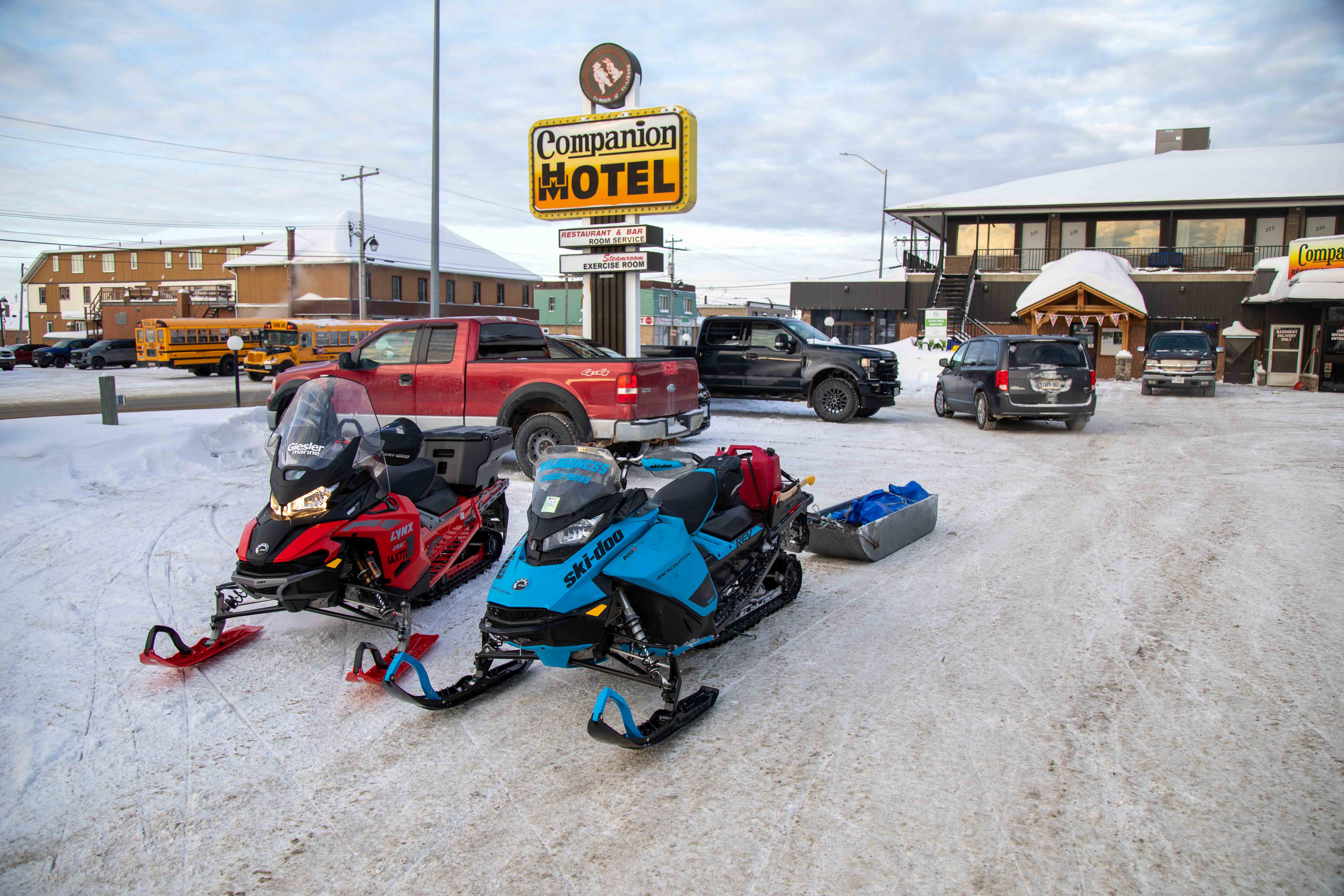two snowmobiles parked in the snowy parking lot in front a a brown building and a sign that says "Companion Hotel"
