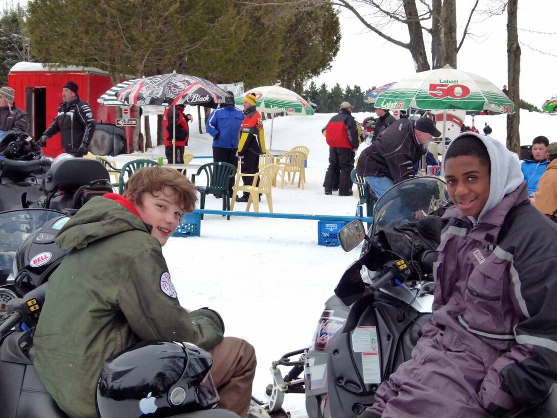 young sledders sitting on snowmobiles with event in background