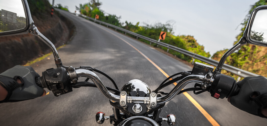 the handlebars of a motorcycle from the driver's point of view, showing the road ahead bending and autumn trees along the side