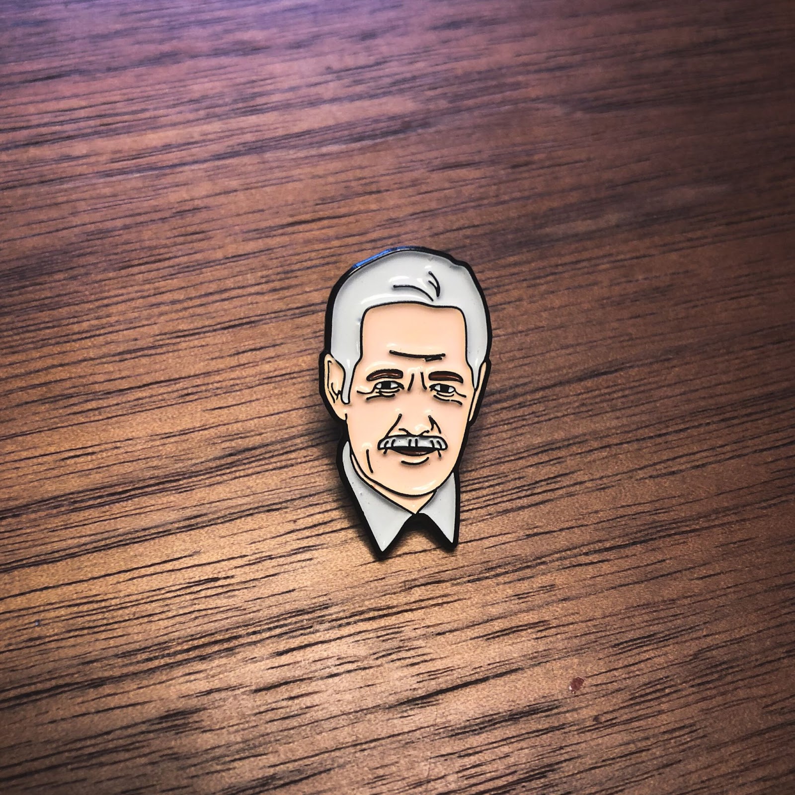 an enamel pin of the head of white-haired, kindly-smiling Alex Trebek