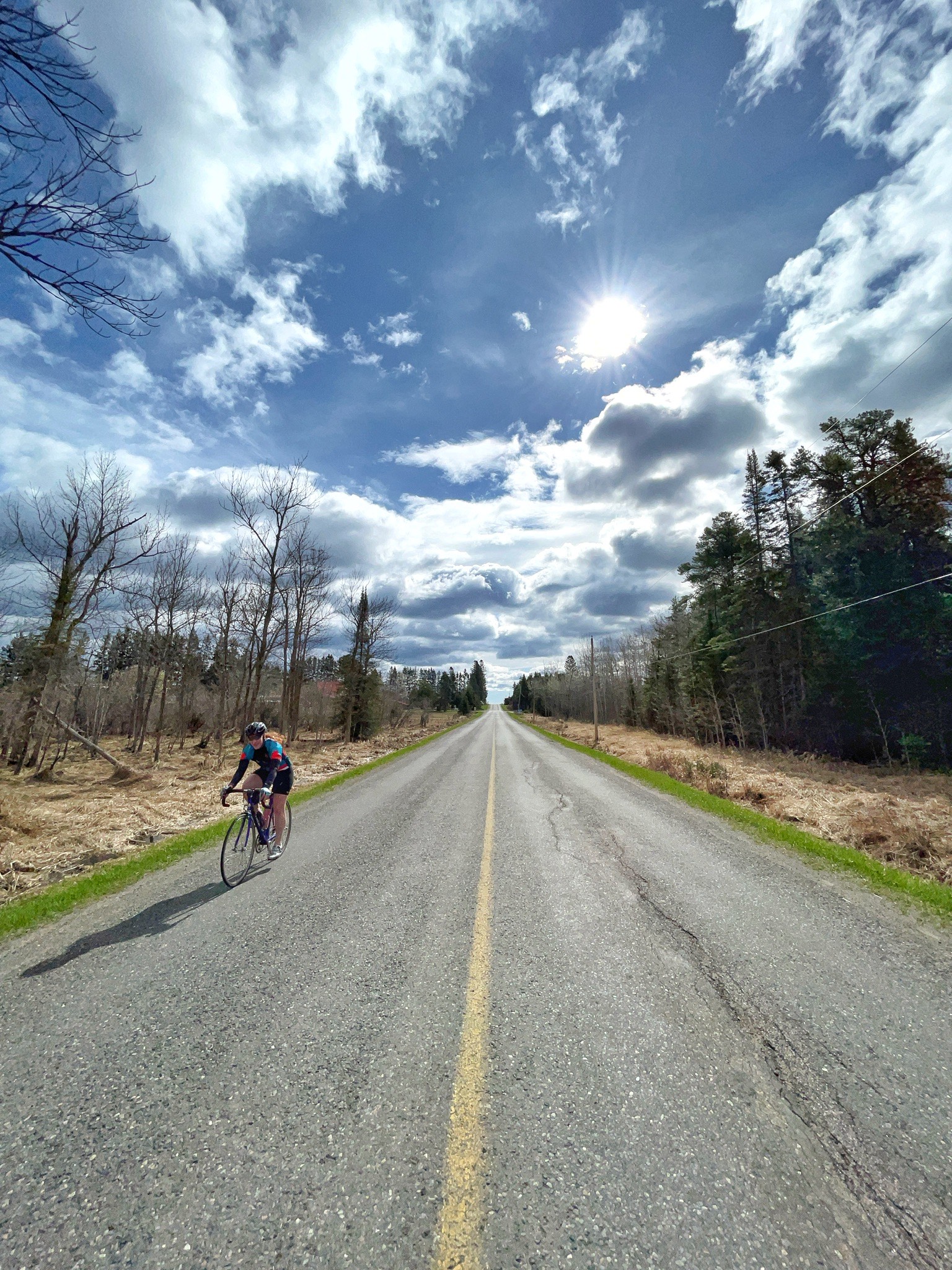 person rides a bicycle down a rural road on a sunny spring day