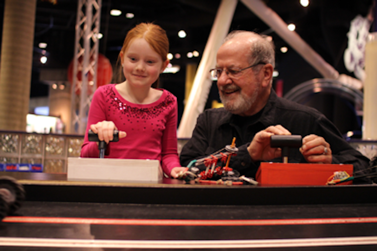 a grandfather and grand daughter smiling and playing with remote train controls at an interactive display at Dynamic Earth