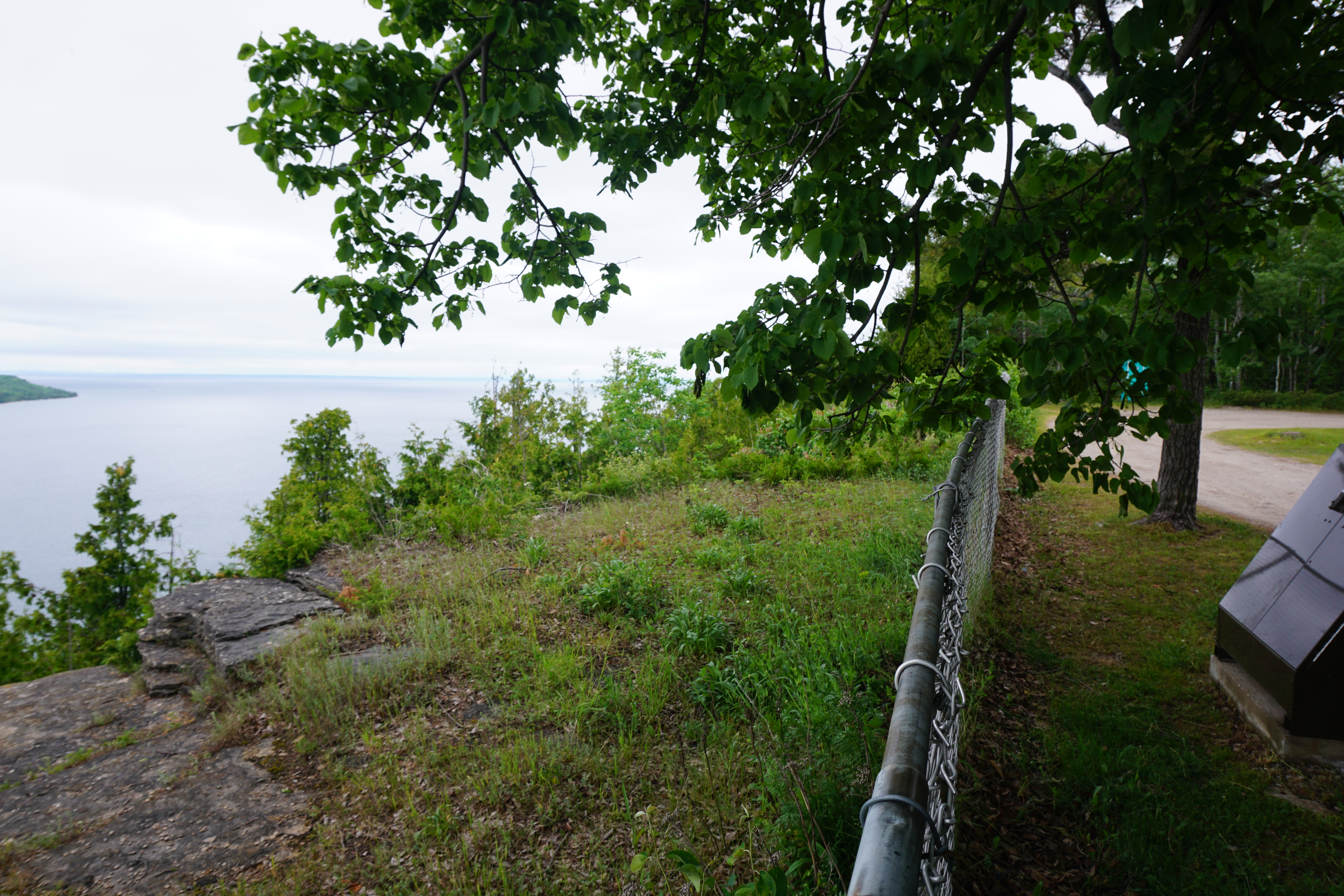 East Bluff Lookout; a green rocky embankment next to a treed walkway, overlooking the broad Gore Bay.