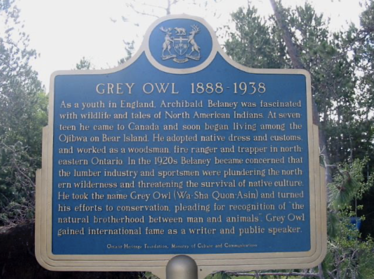 The Grey Owl plaque in Finlayson Point Provincial Park; a blue and silver informational plaque in front of tall green trees.