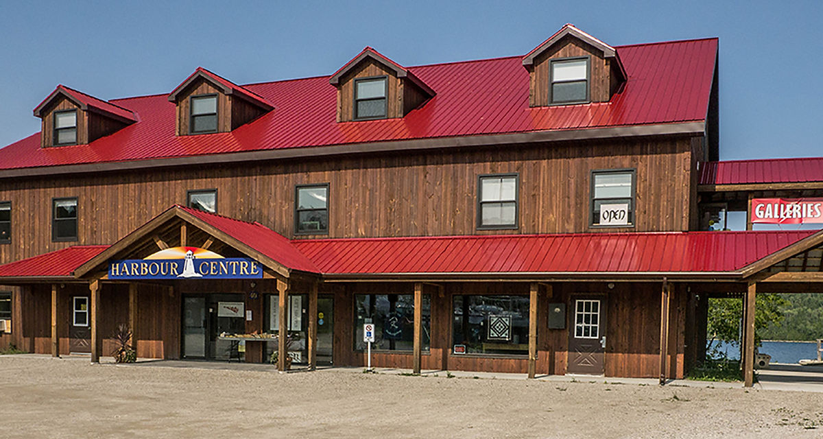 Harbour Centre in Gore Bay; a large, pretty two-story wooden building with a red roof next to the bay.