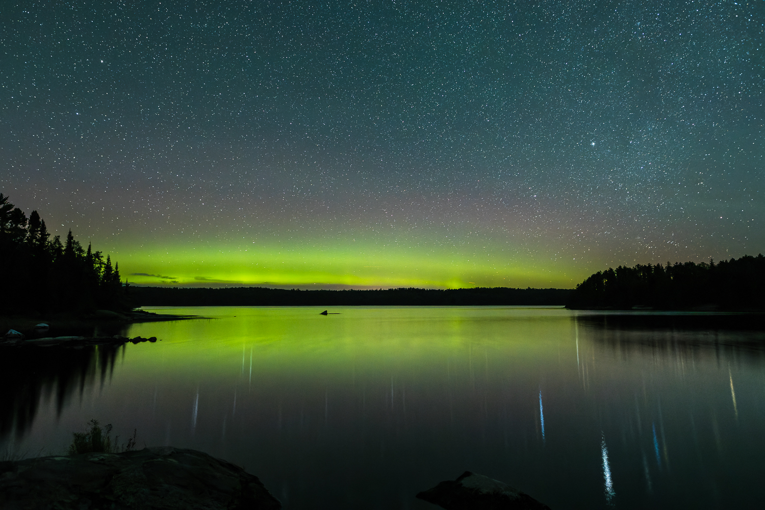 starry night skies and northern lights over a lake at Quetico