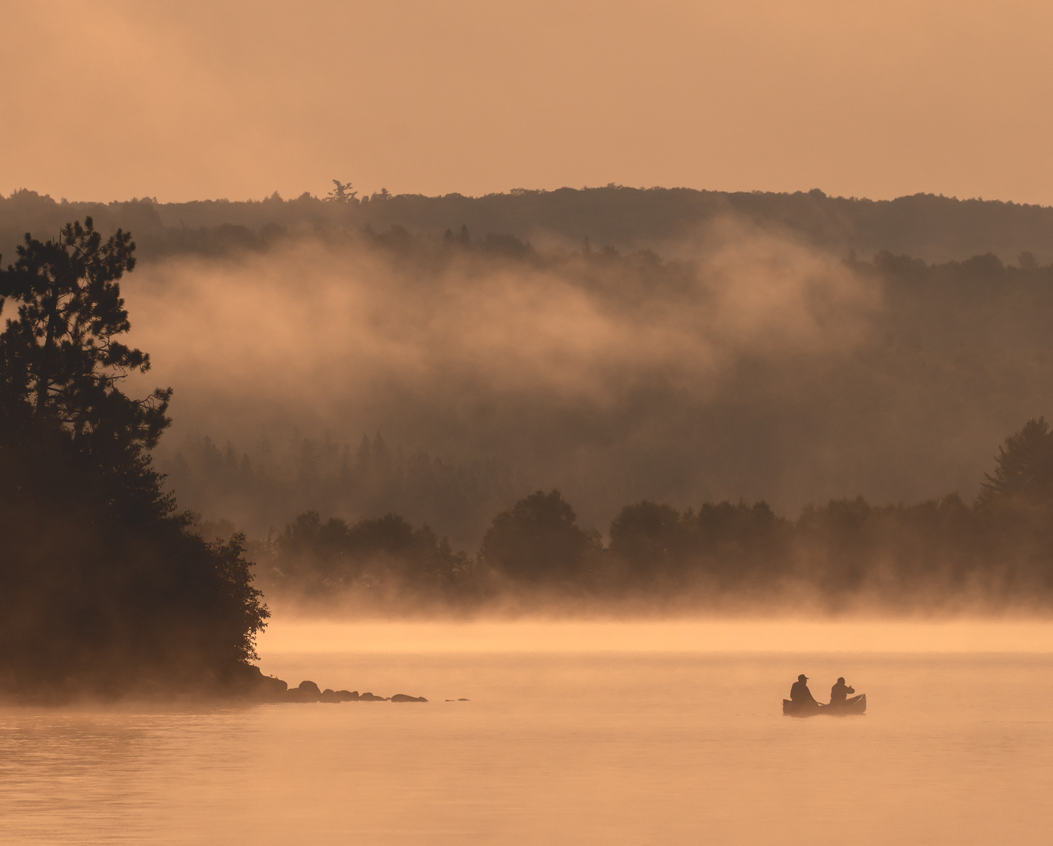 two canoeists on misty water at dusk