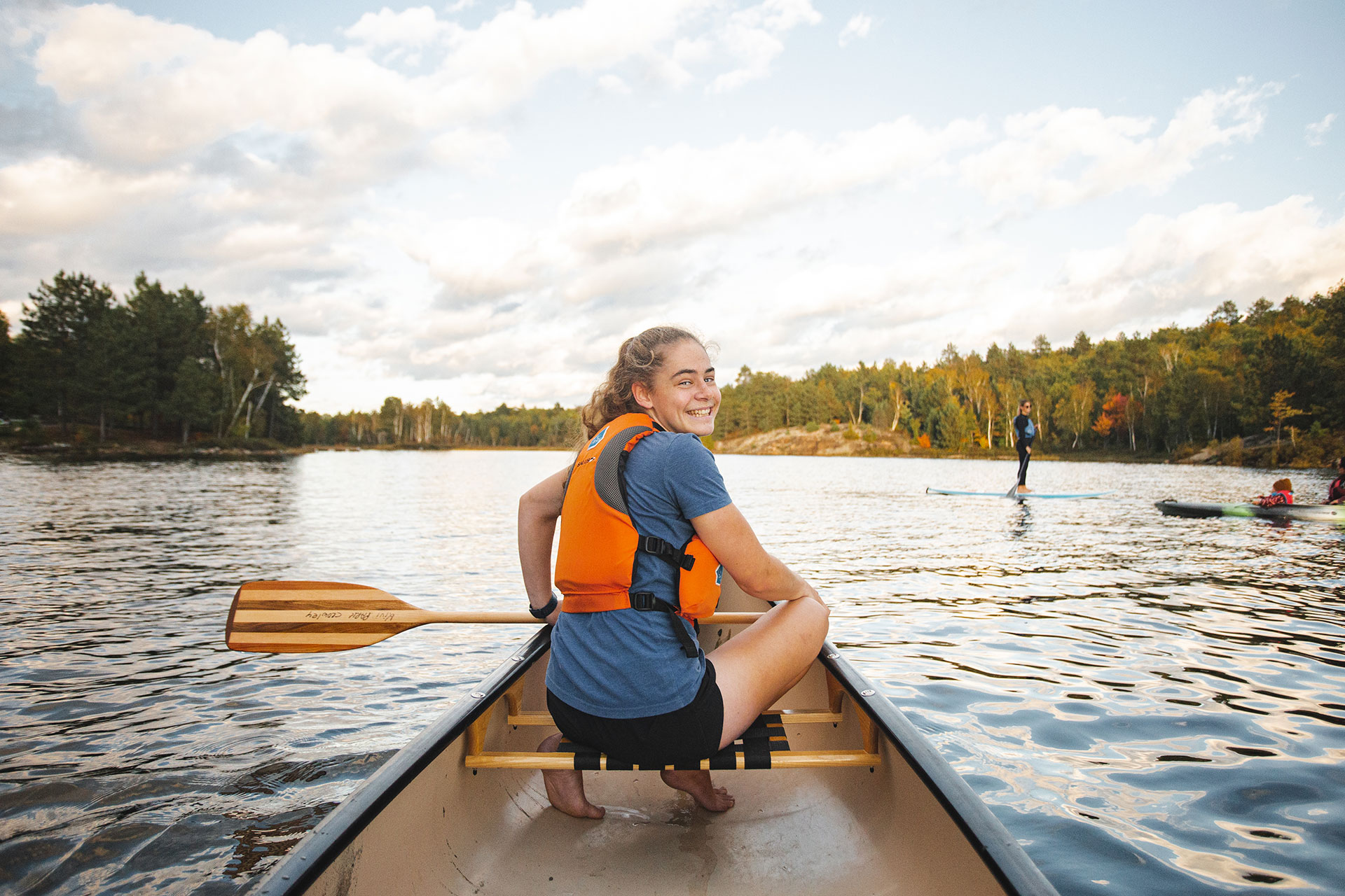 girl turns around and smiles while paddling in the bow of a canoe