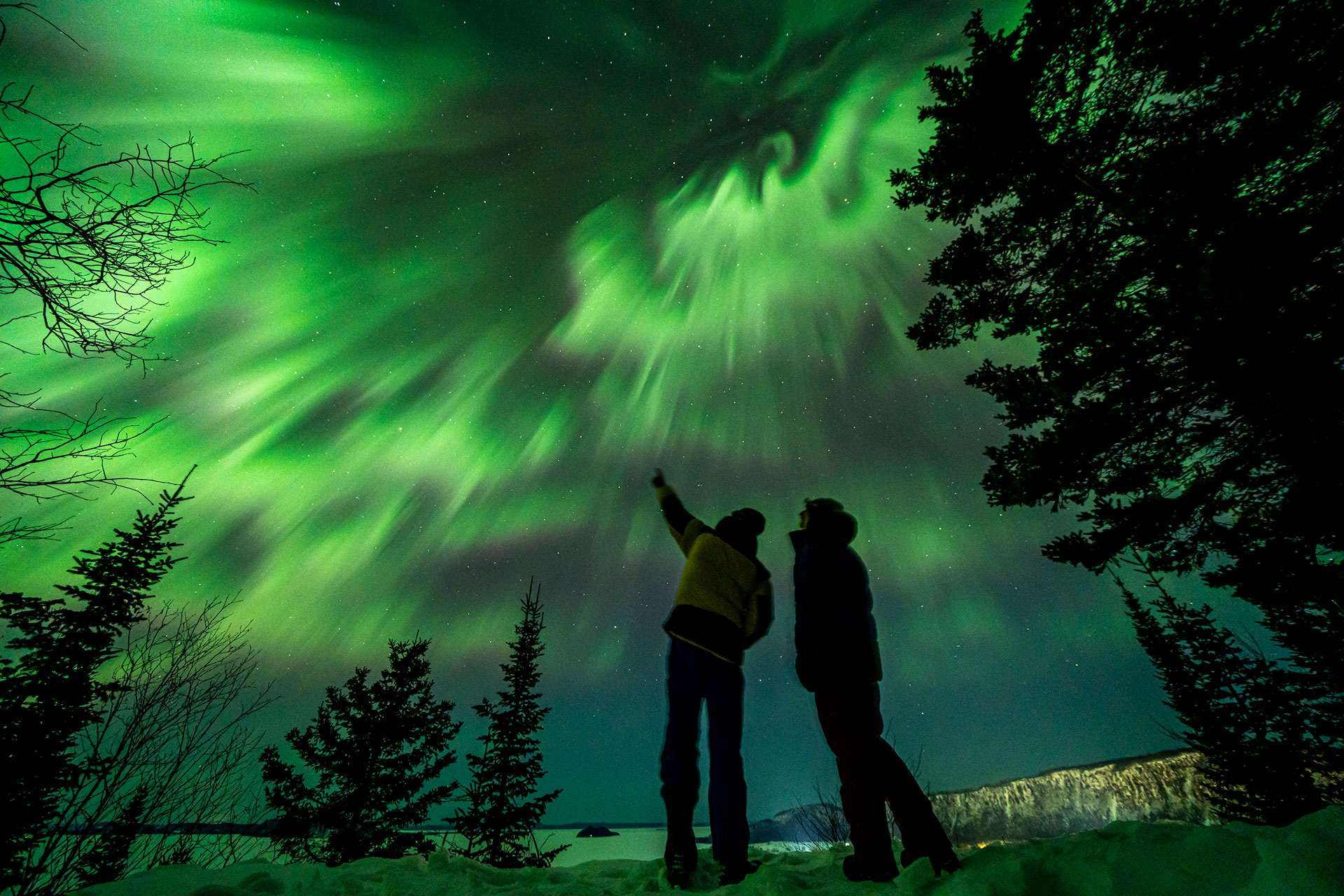 two people stand and point at the Northern Lights