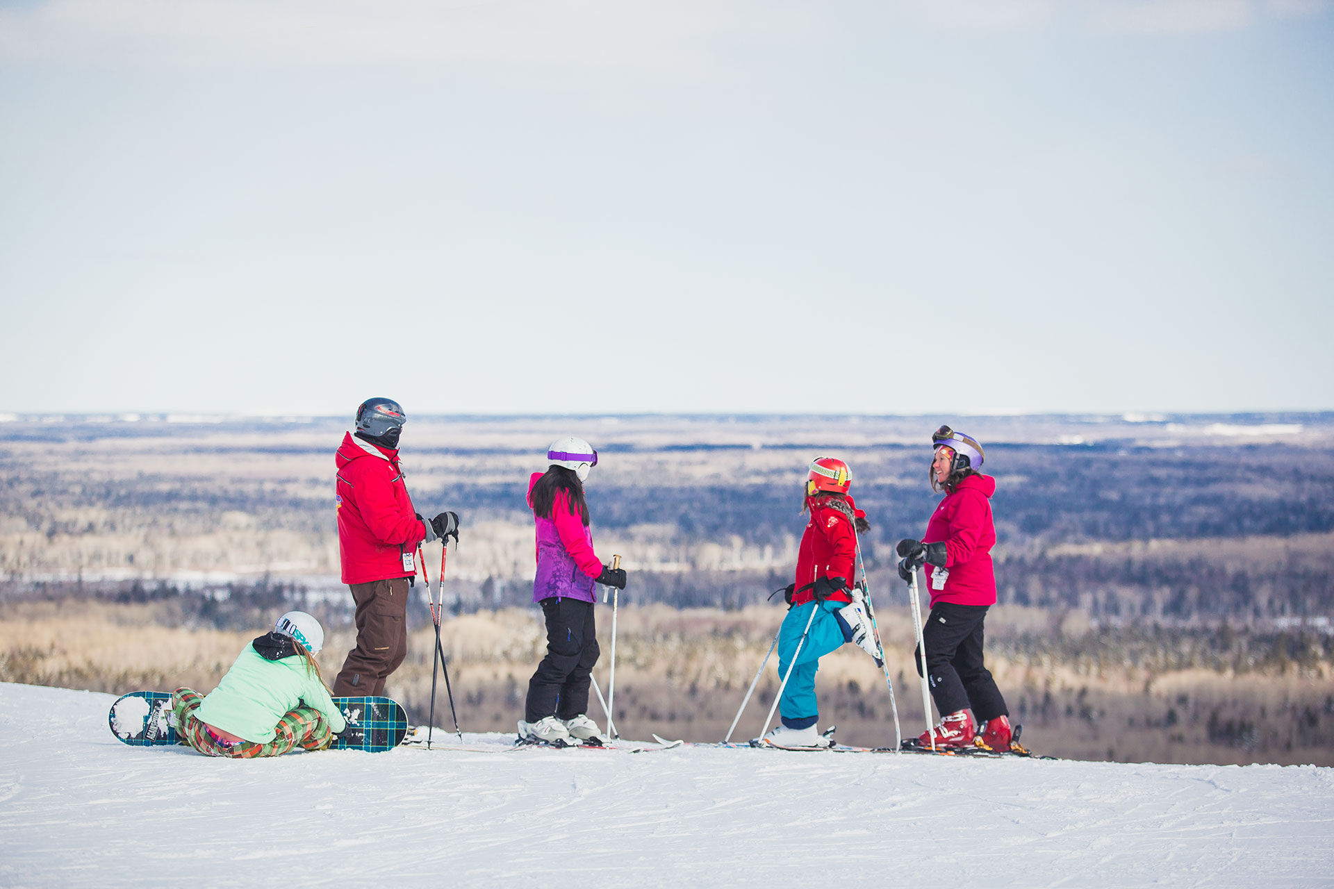 a family of four skiers and one snowboarder prepare to start a downhill run