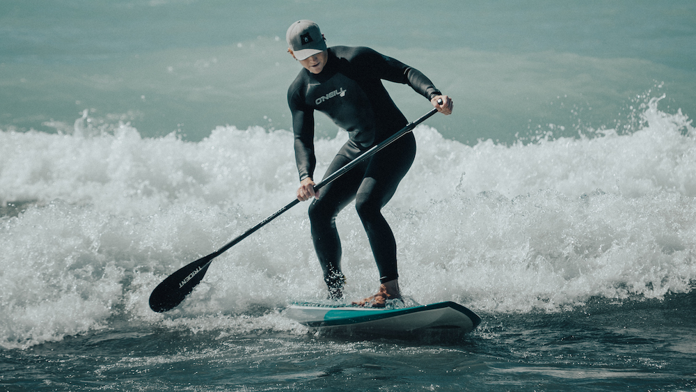 Man wearing wetsuit and ball cap surfing on a SUP