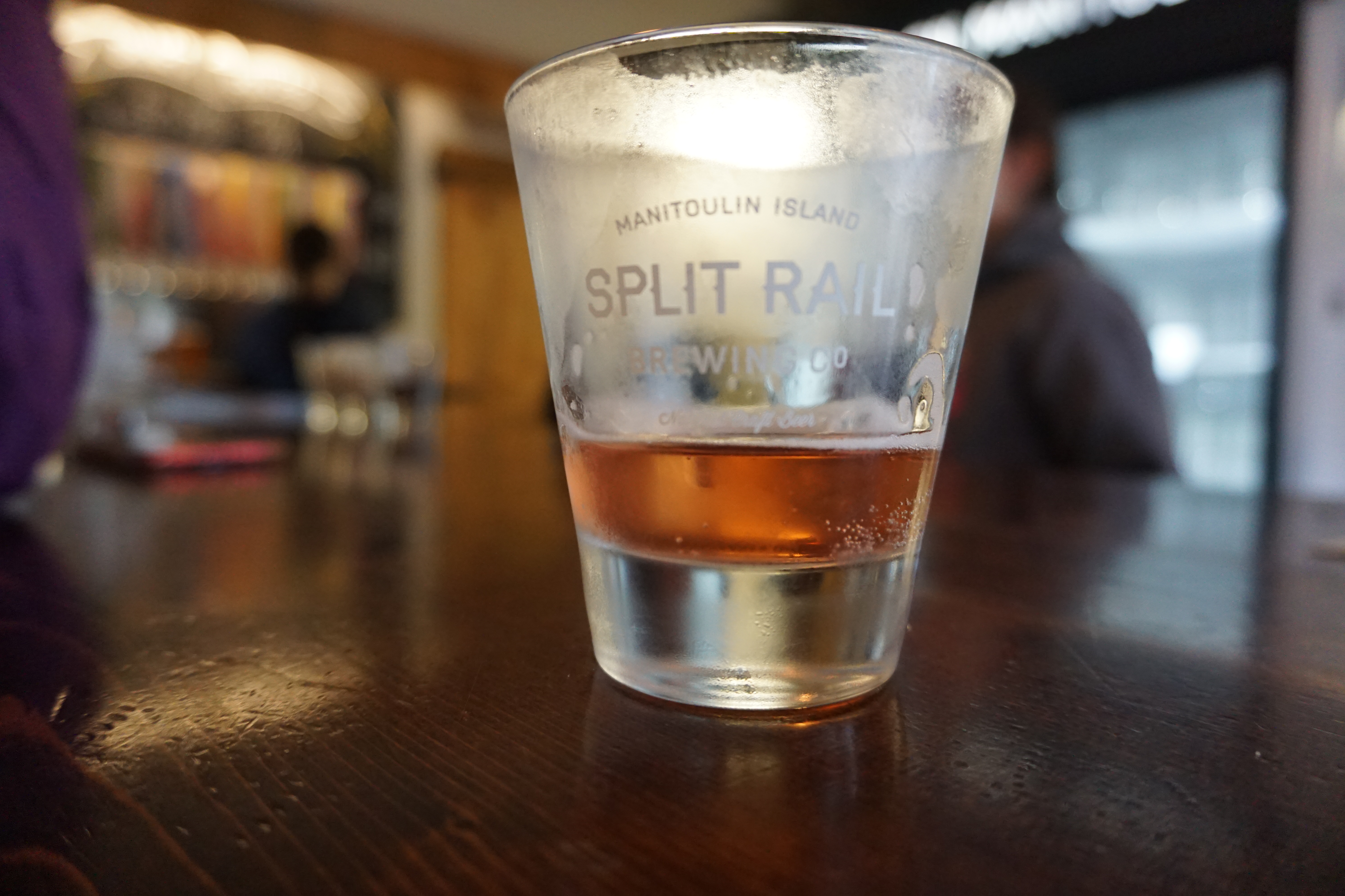A nearly empty, frosted glass on a table with "Split Rail" printed on it.