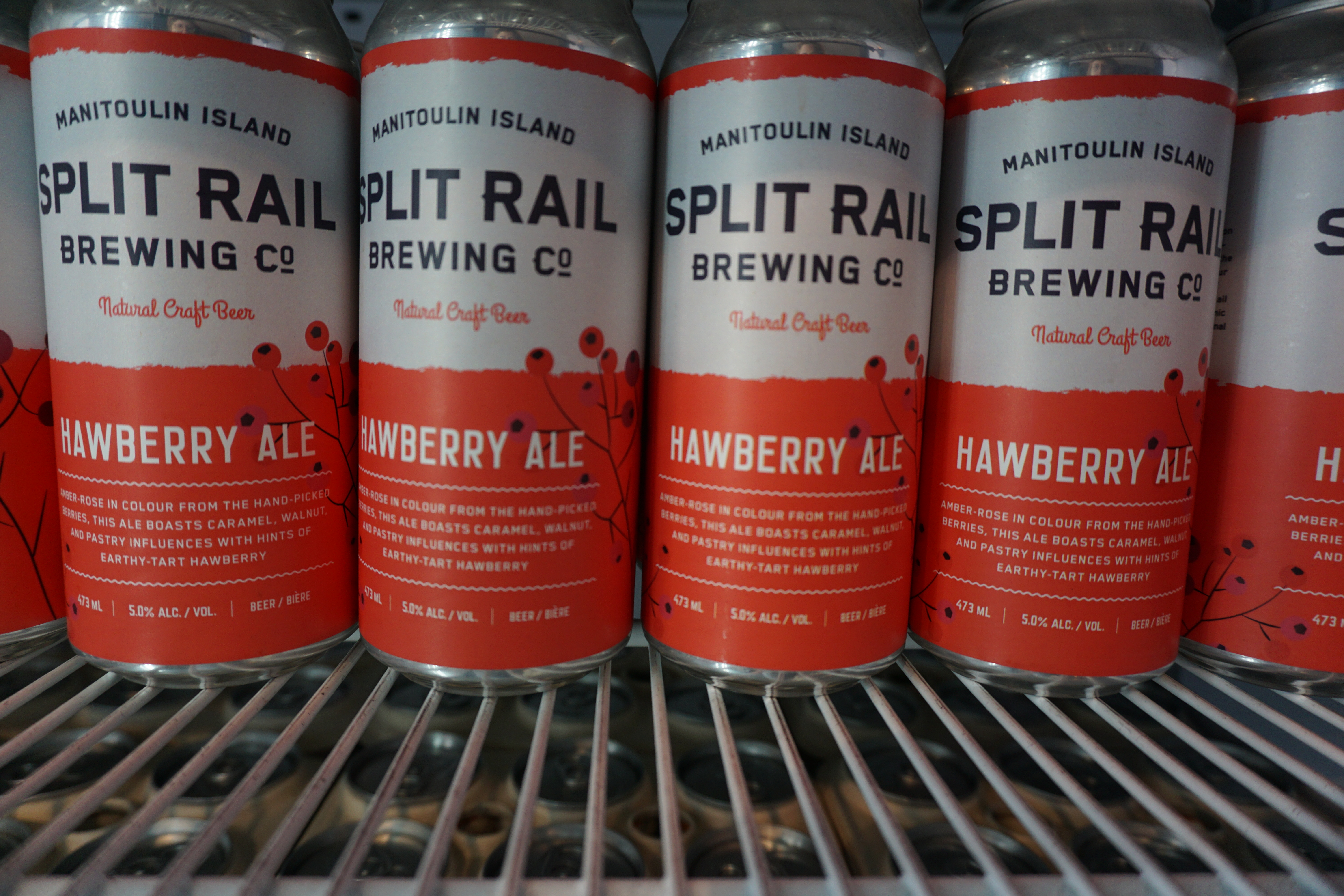 Rows of red and white cans of Split Rail Hawberry Beer in a cooler.