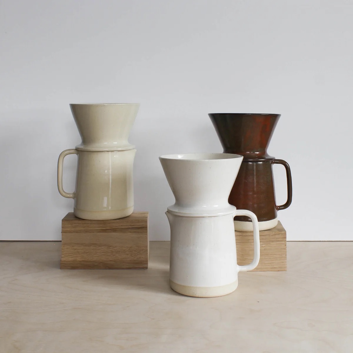 3 pourover coffee sets in white, cream and dark brown, displayed with small wooden boxes.