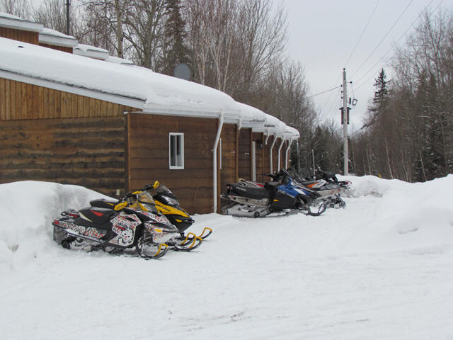 several snowmobiles parked next to a snowy wooden cabin