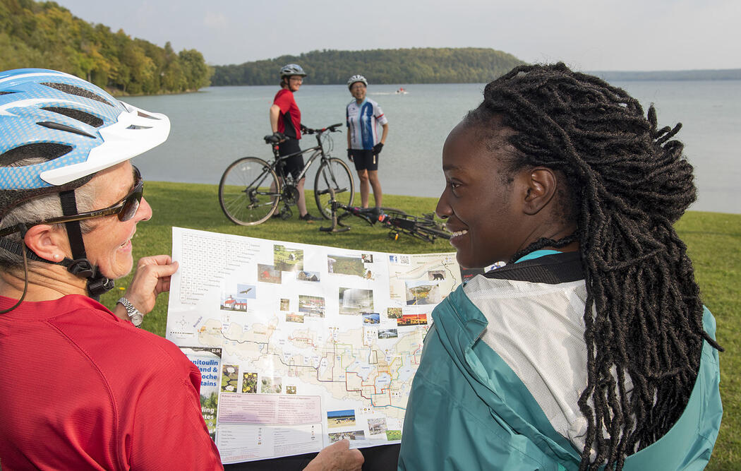 cyclists look at a cycling map while standing along the shoreline of Manitoulin Island