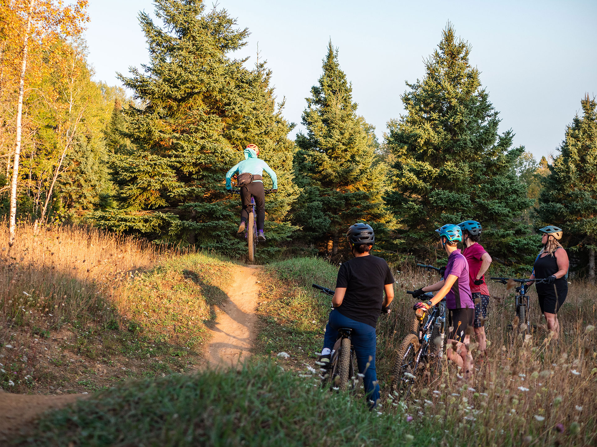 one young cyclist rides on a dirt trail while others watch