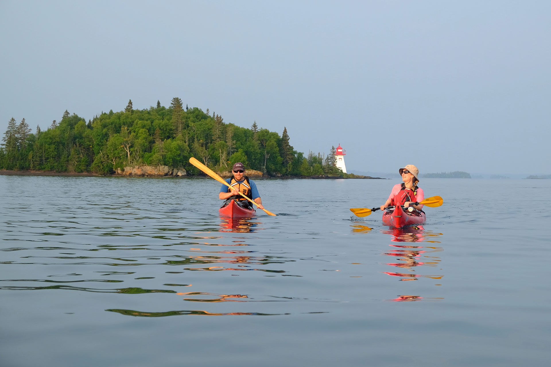 two people paddle on Lake Superior with an island lighthouse behind them