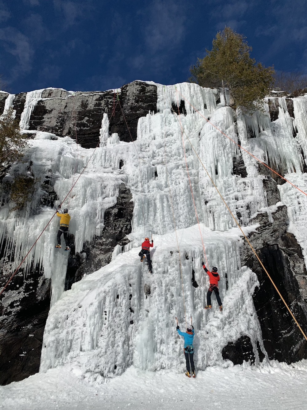 Four people climbing up frozen waterfall in the winter.