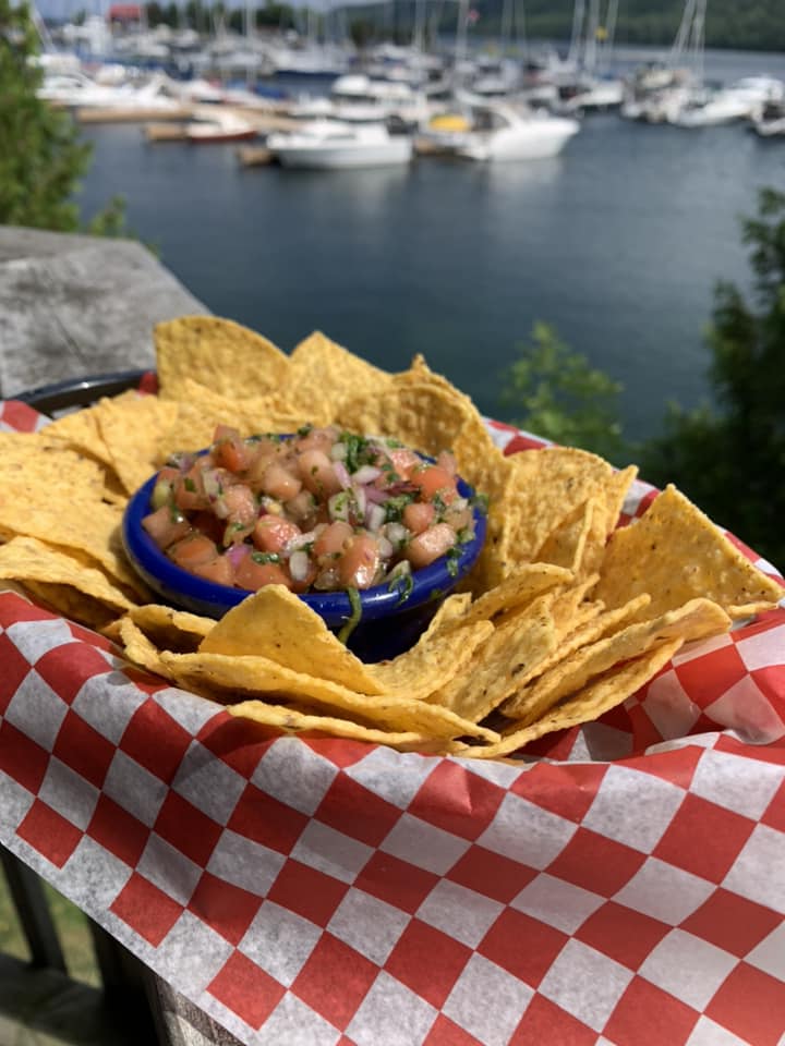 an order of tortilla chips and salsa on a deck rail in front of a boat-filled harbour.